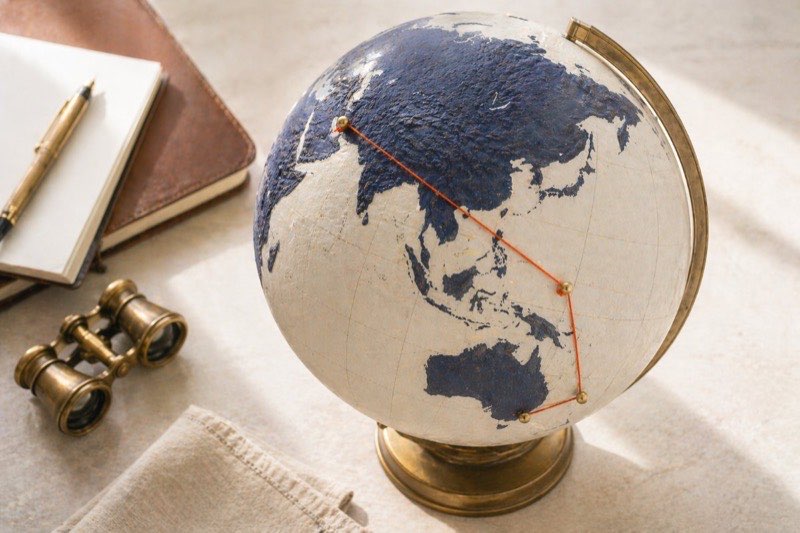 Vintage world globe with brass pins and an orange thread tracing an ultra-long-haul flight route