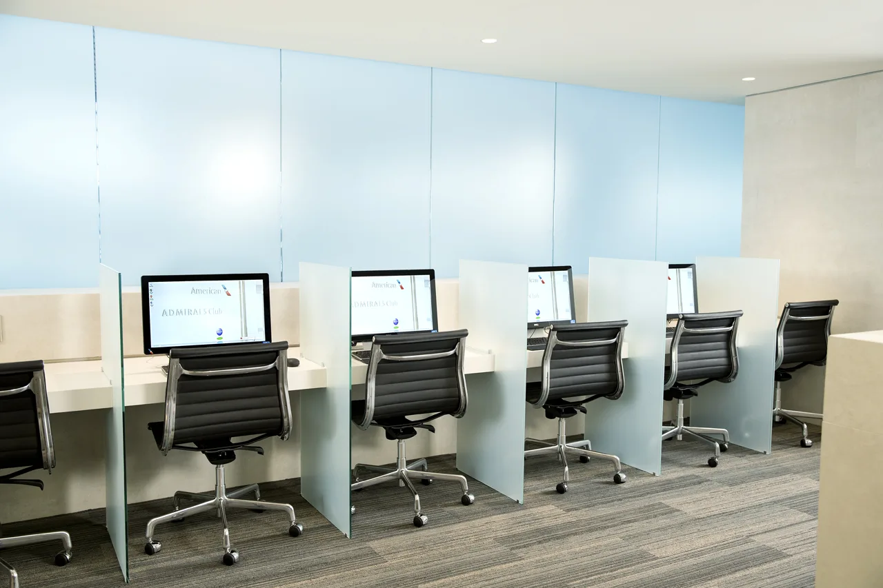 A row of private airport lounge workstations with glass dividers, where a traveller can read a programme terms page before applying.