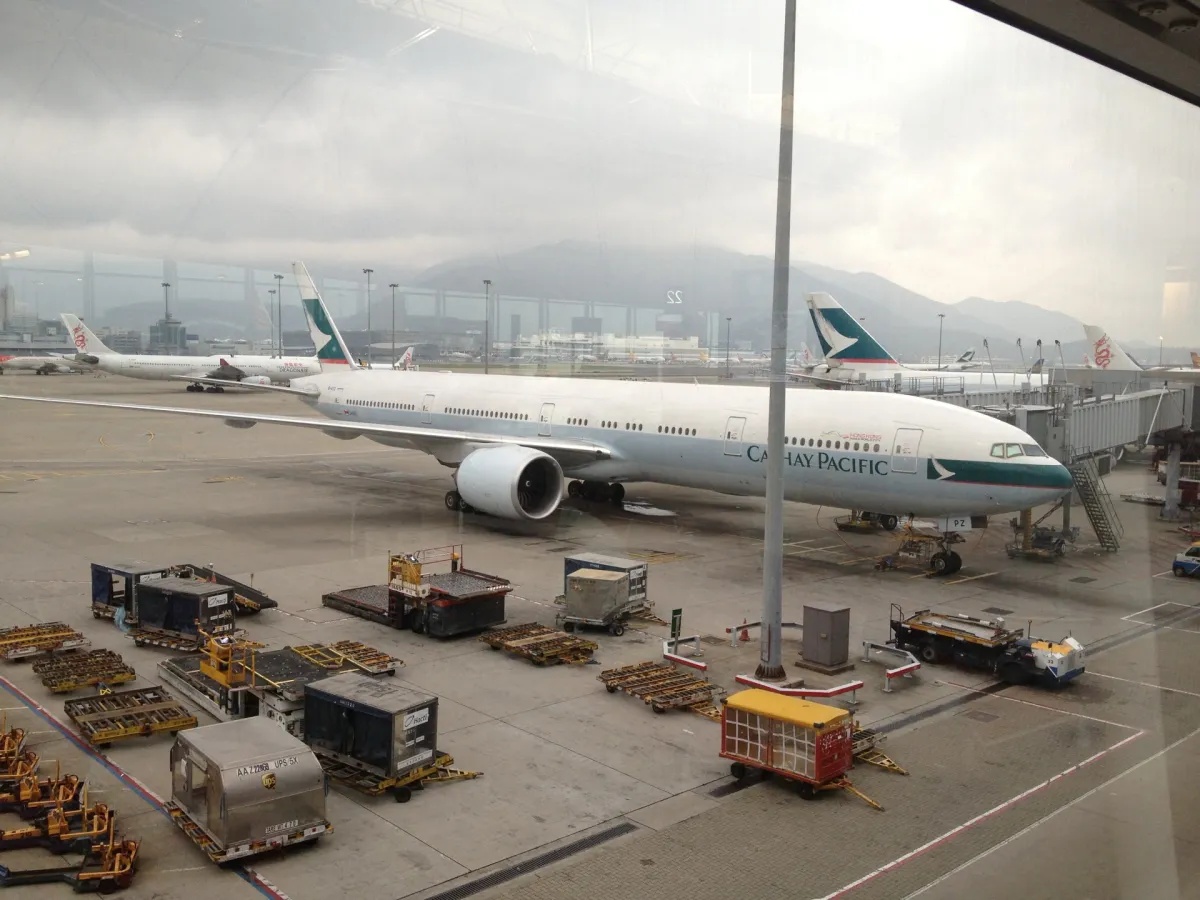 Cathay Pacific Boeing 777-300ER at Hong Kong International Airport seen through terminal glass, with misty mountains behind