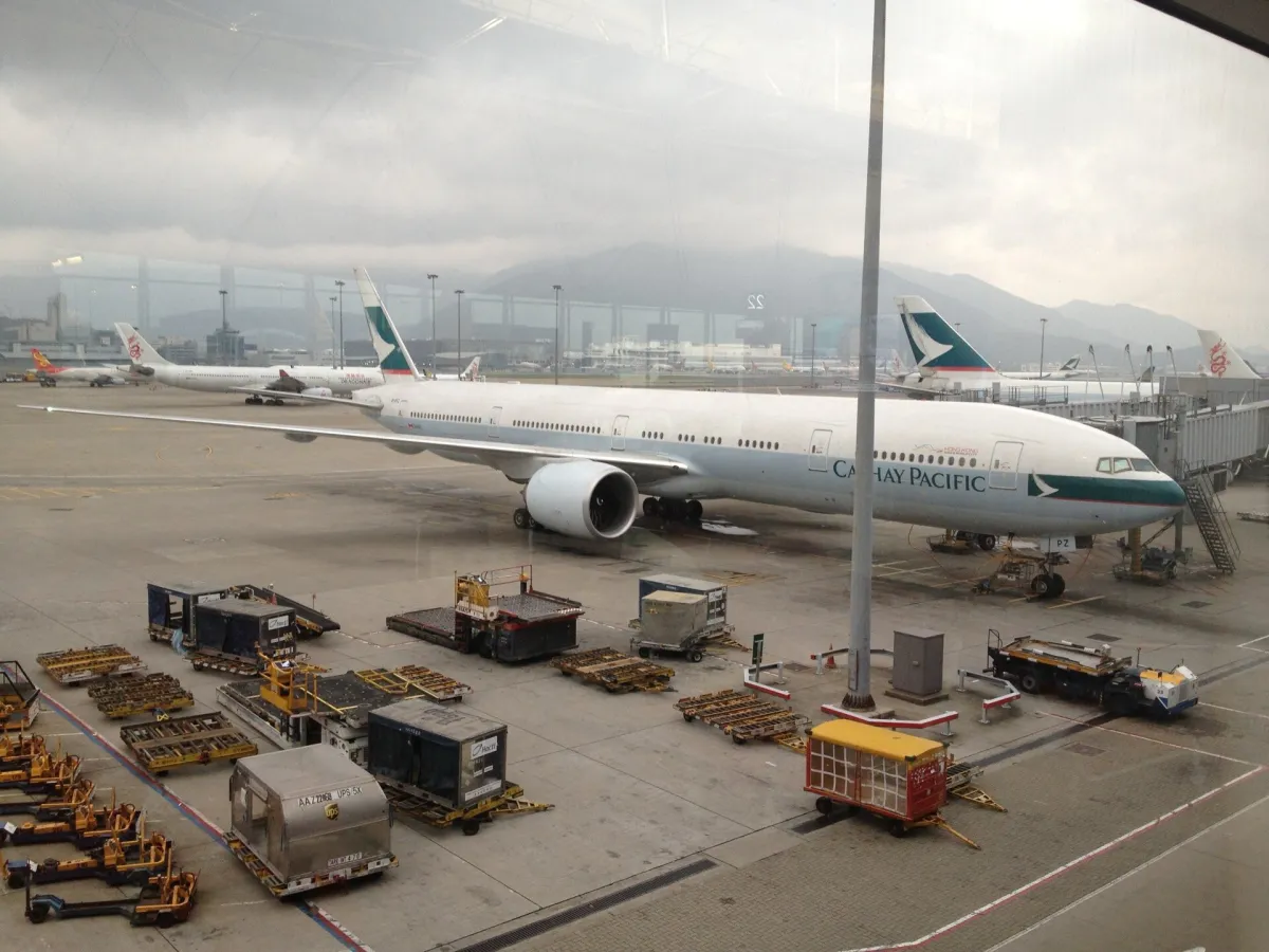 A Cathay Pacific Boeing 777-300ER at Hong Kong International Airport seen through terminal glass on an overcast day