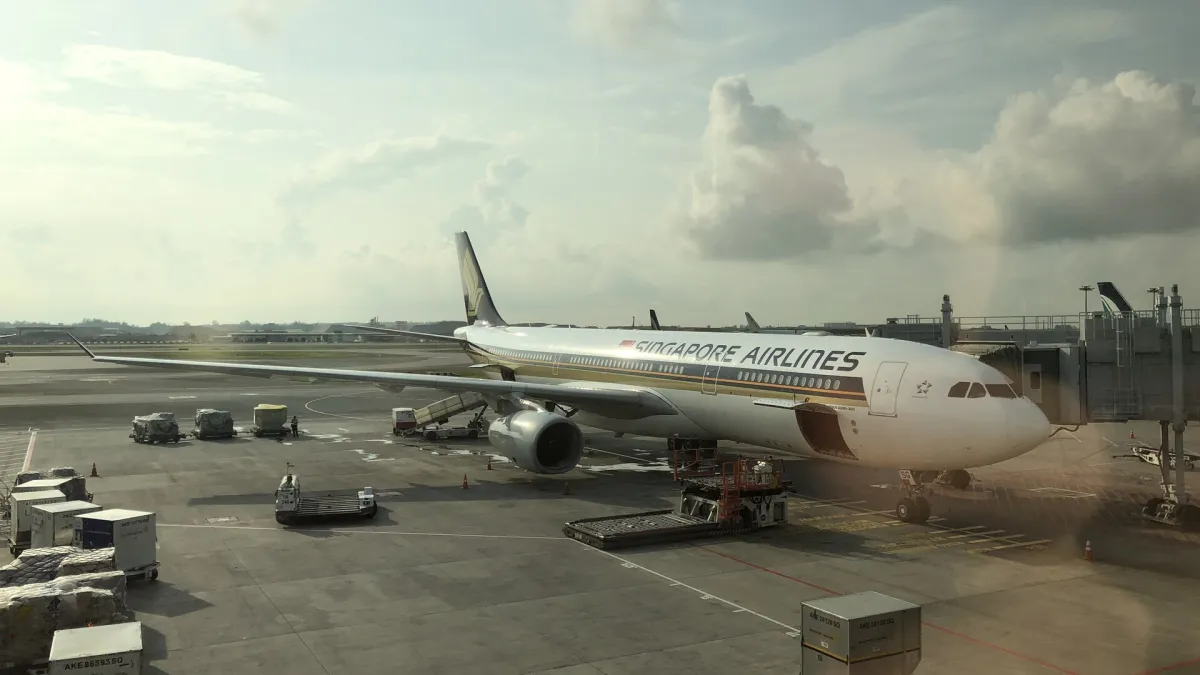 A Singapore Airlines Airbus A330 being serviced at a gate at Singapore Changi Airport, white and gold livery against a blue sky with cloud